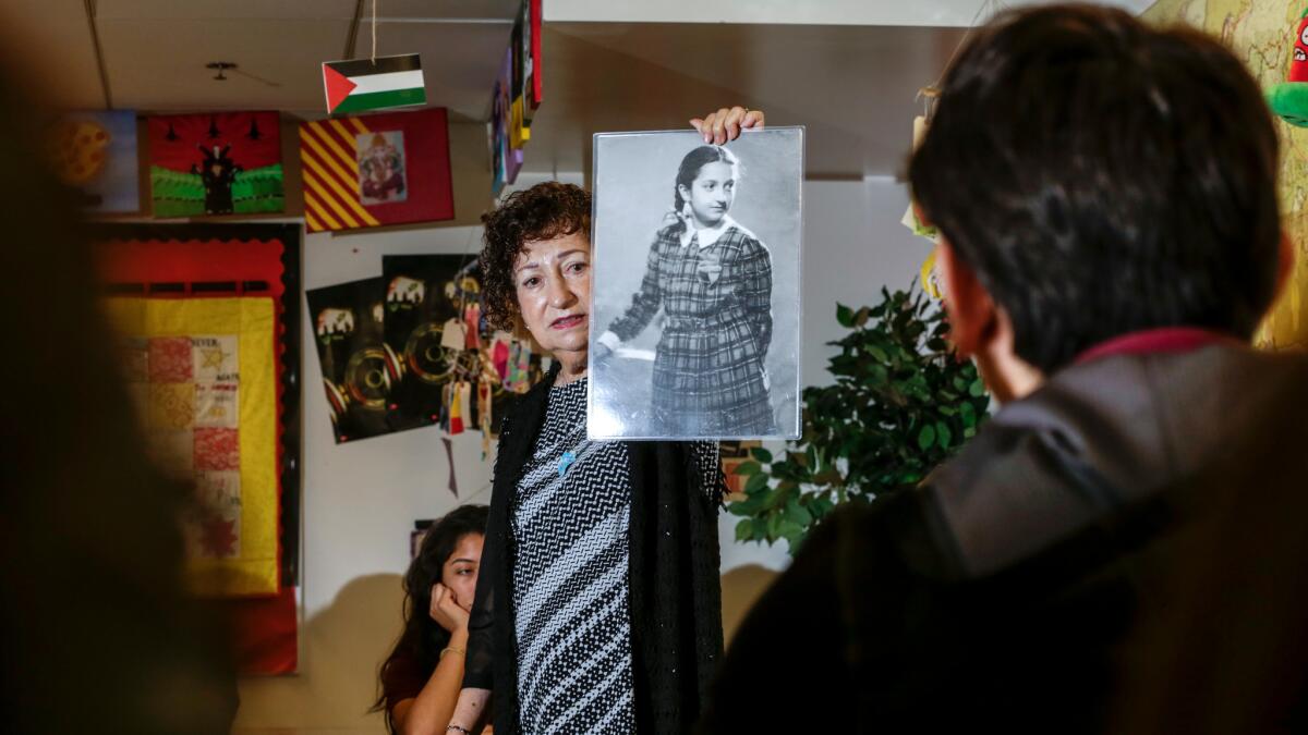 Gabriella Karin stands before a classroom and holds up a photo of herself as a girl