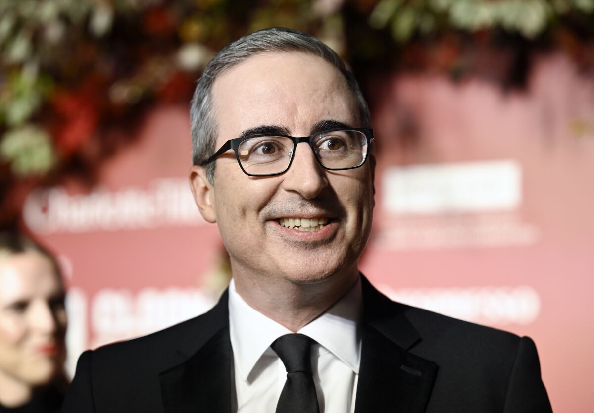 A man with short gray hair and glasses smiling in a black suit and tie