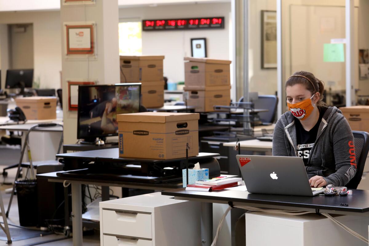 A masked woman works in an empty office.