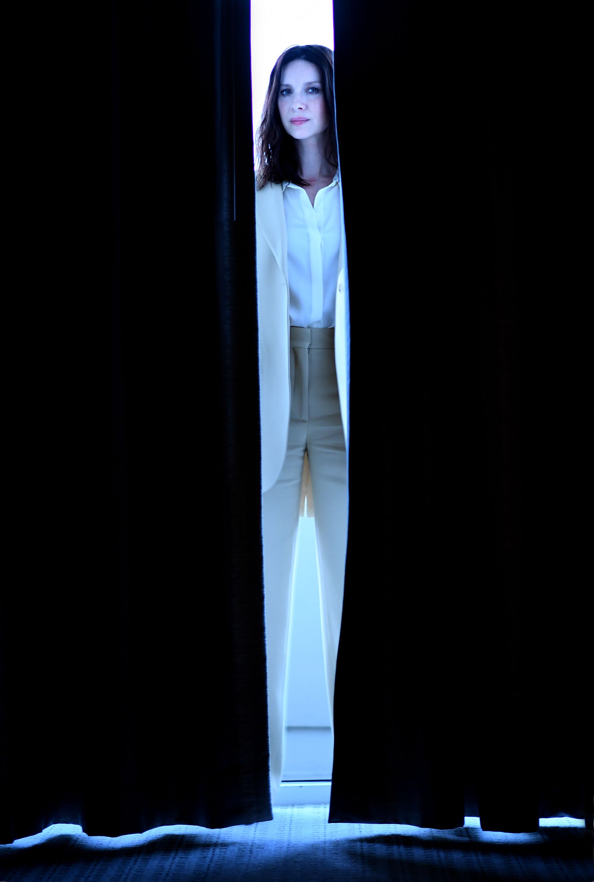 A woman stands in the gap between two dark drapes