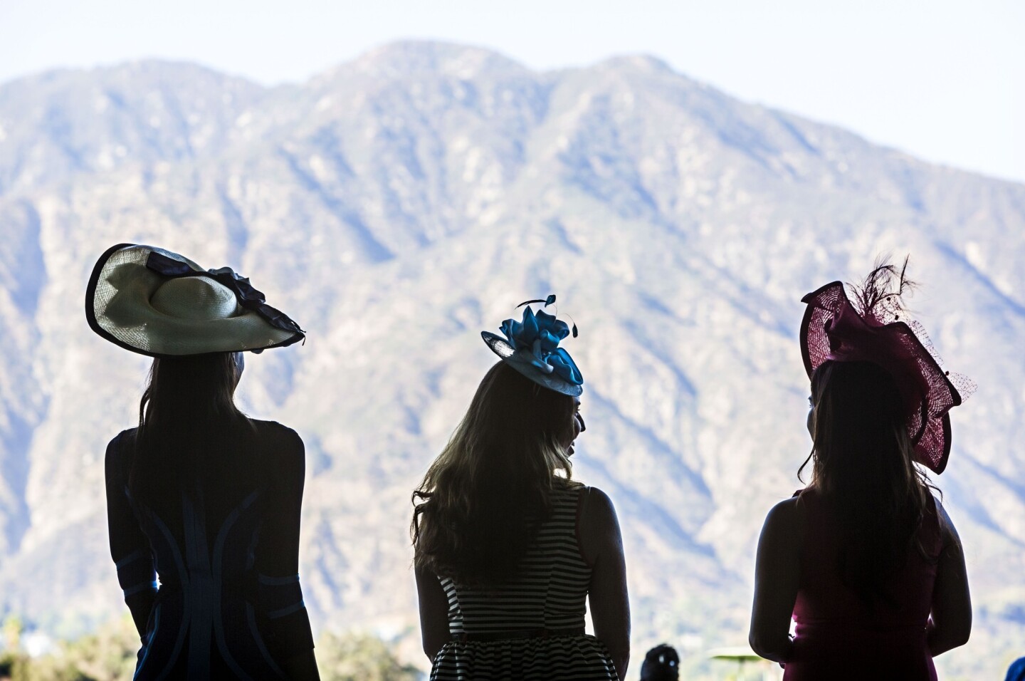 Models Jo Scott, Bailey Gallison, and Natalie Resendiz posing and wearing hats by Christine A. Moore Millinery at Santa Anita Park, against the backdrop of the San Gabriel Mountains.