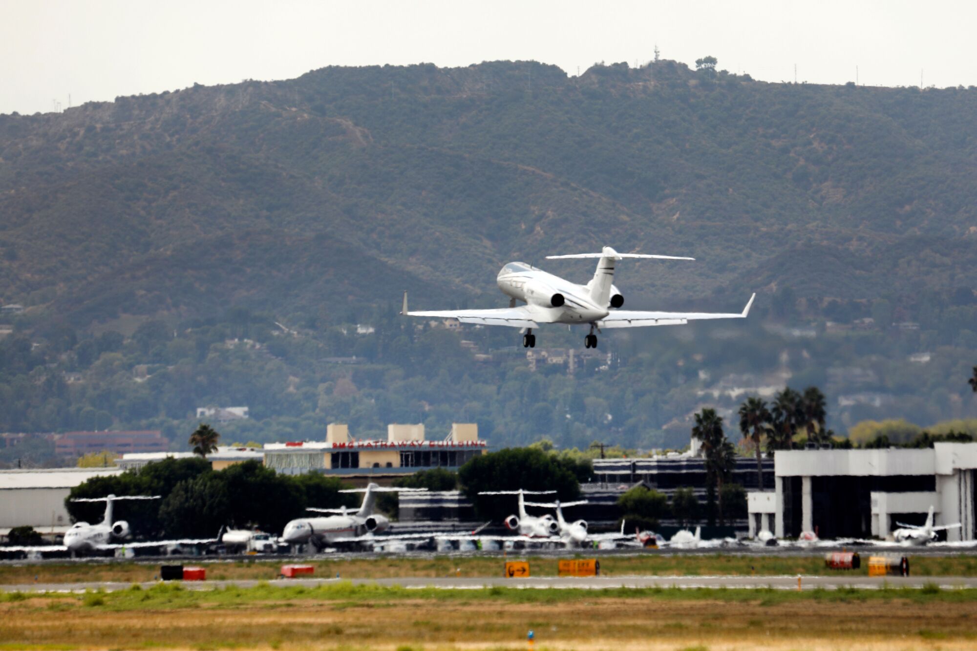 A private jet takes off from a runway at Van Nuys Airport, with the Hollywood Hills visible in the distance.