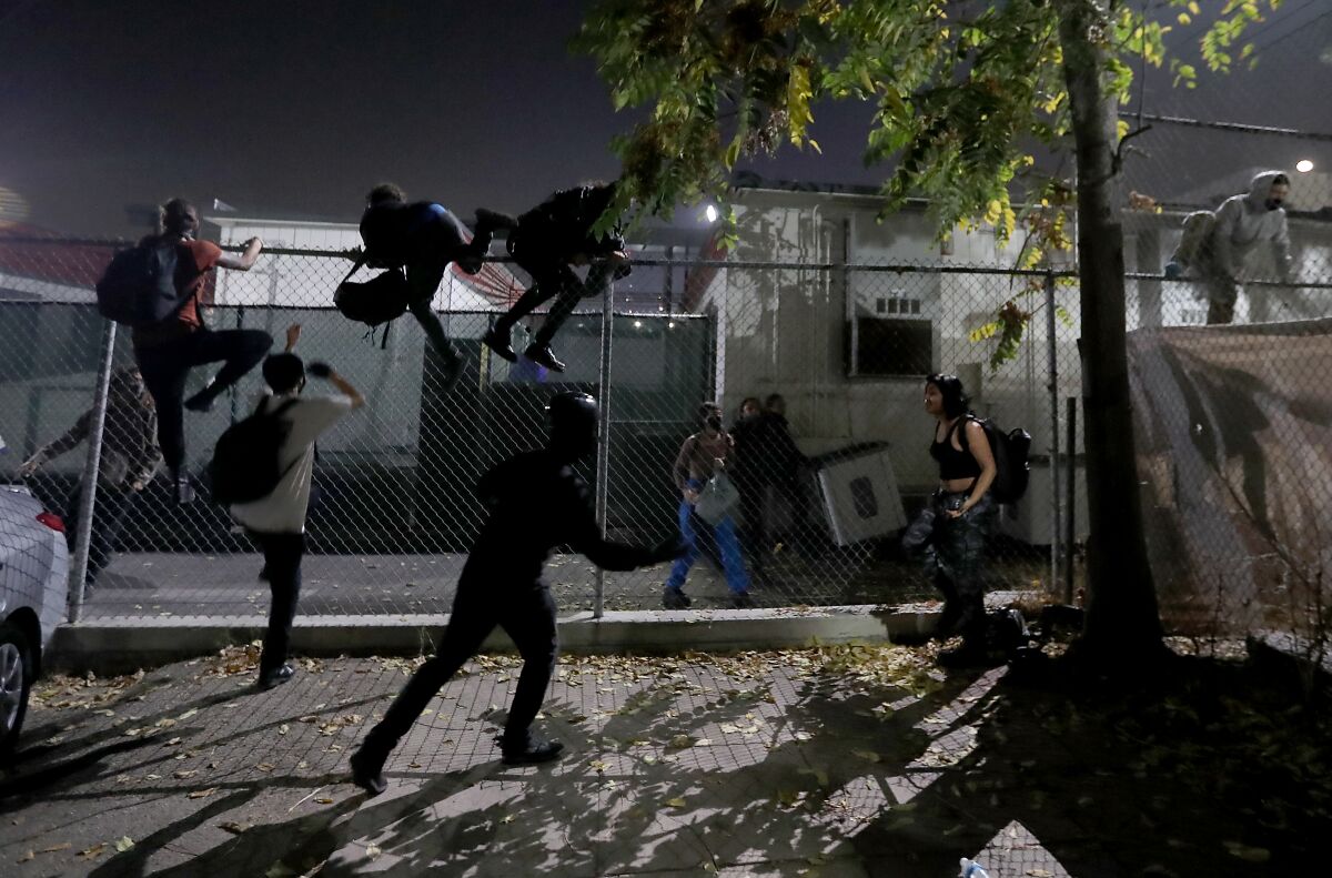 Protesters jump a fence to get away from LAPD officers after getting hemmed in at 18th and Figueroa streets