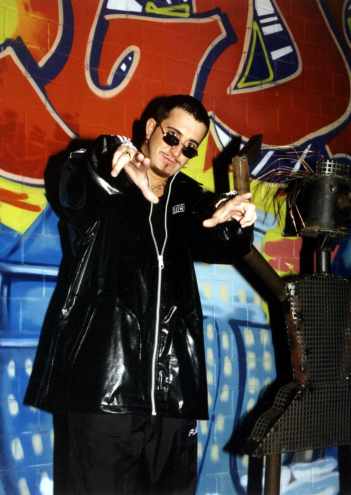 Brian Gillis points at the camera wearing sunglasses and a black leather jacket. 