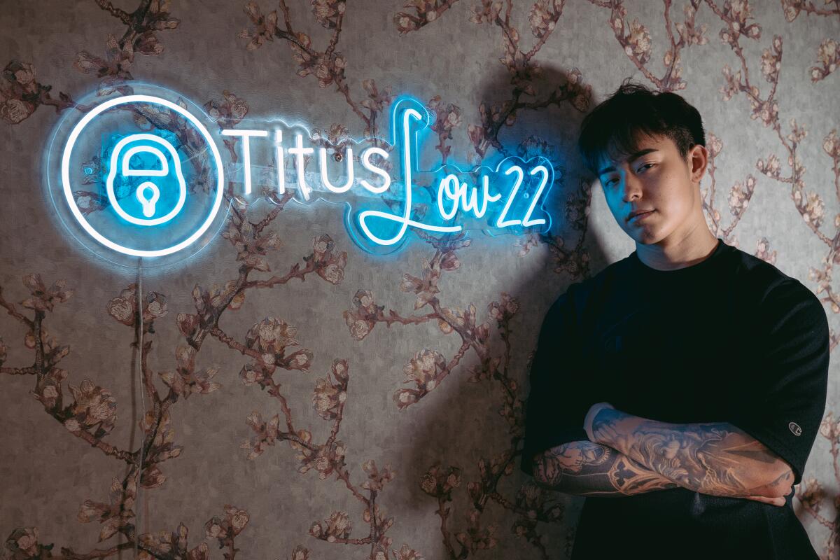 Titus Low posing next to his user name for his Onlyfans account and Twitter: @Tituslow22, a signage his artist friend made.