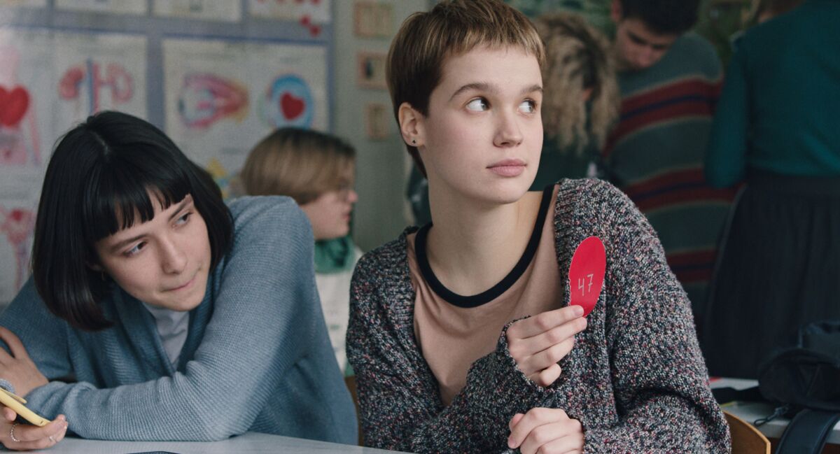 Two teen girls sit in a classroom.