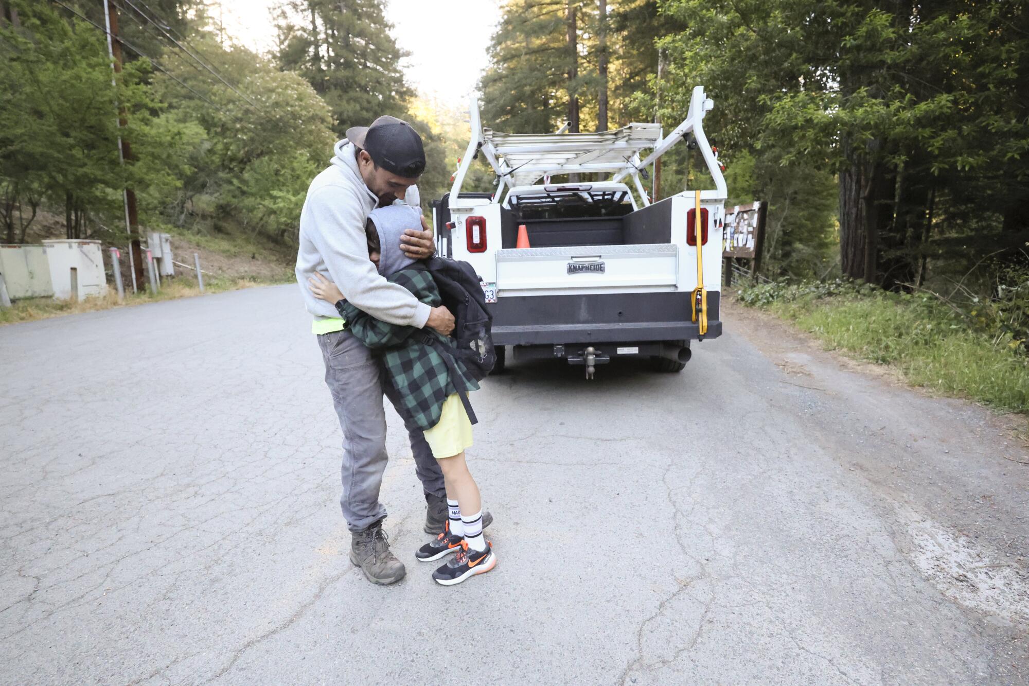 An adult hugs a child in front of the back of a truck.