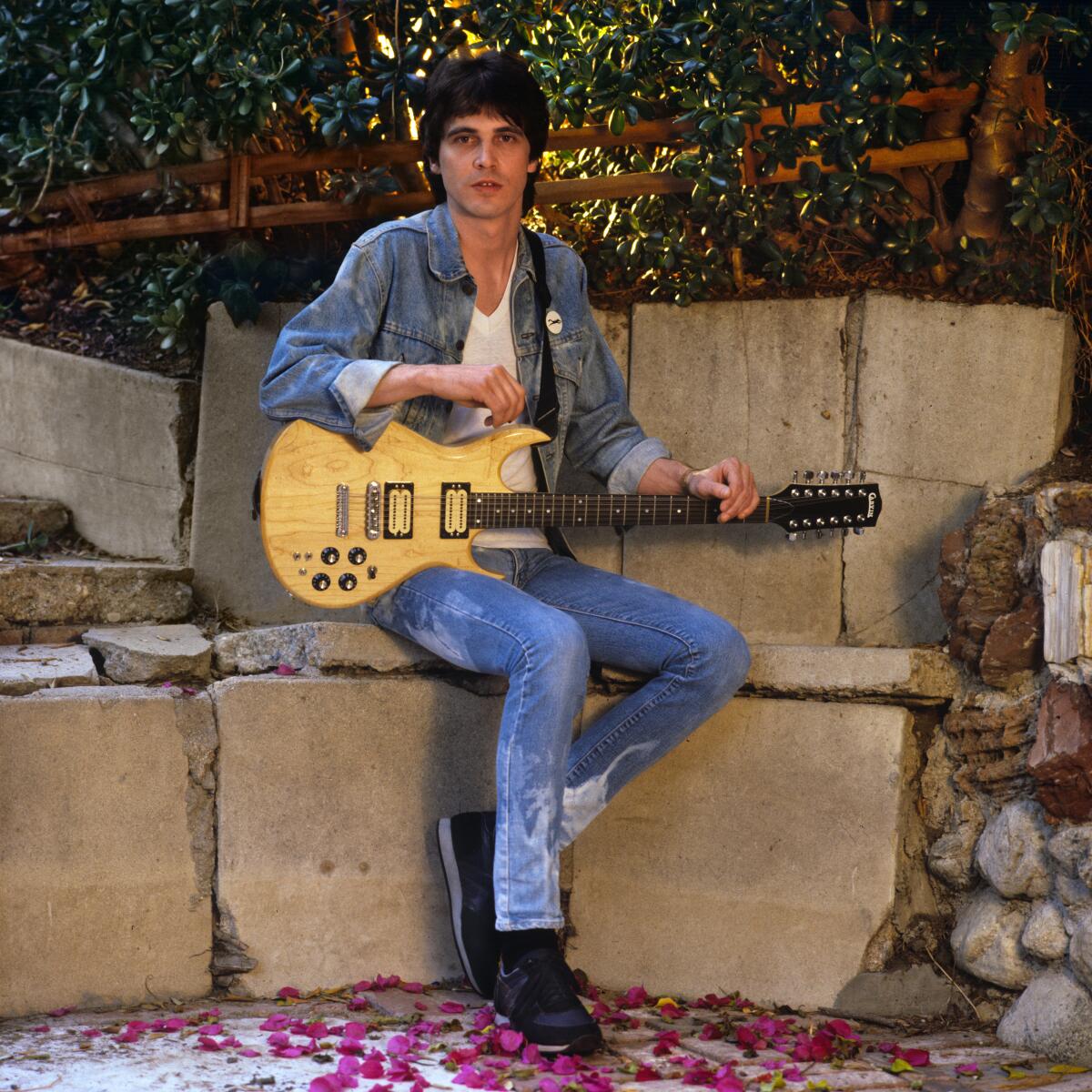 A singer-songwriter holds an electric guitar while seated outside 