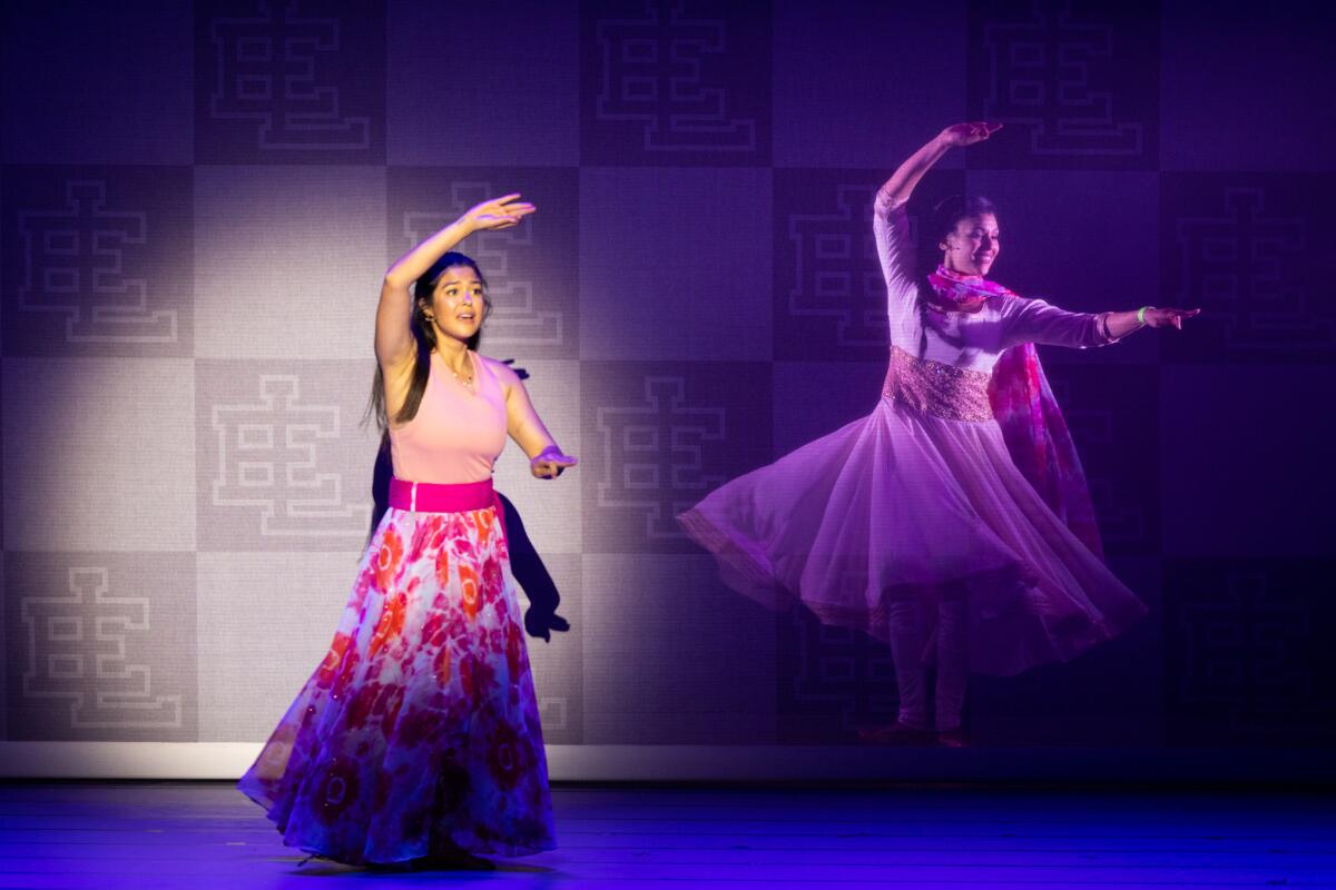 A girl onstage in a pink floral skirt and pink tank, in a ballet pose, next to an apparition of a dancer in the same pose