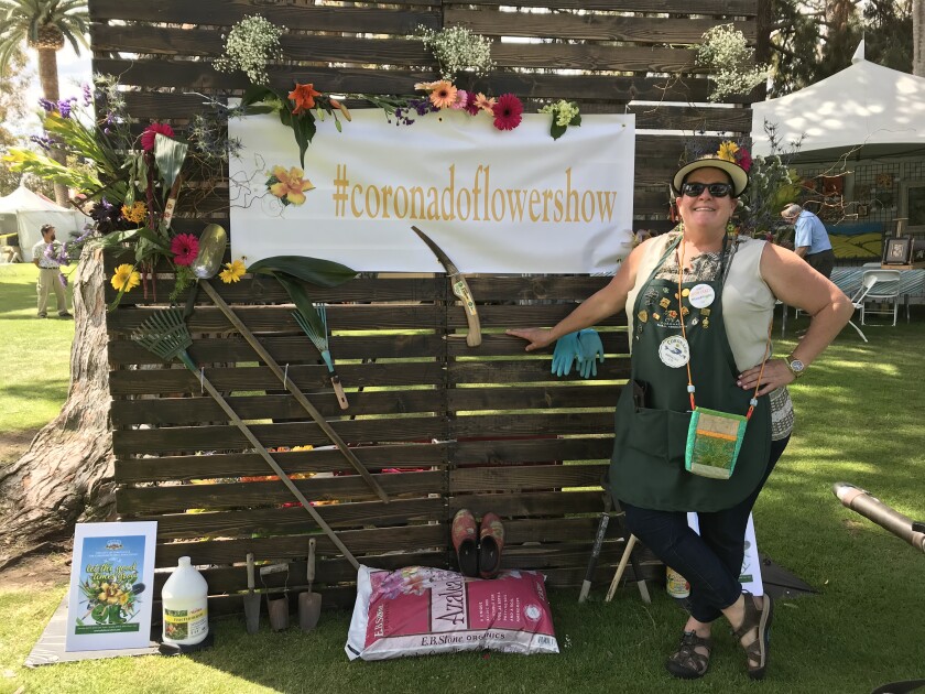 A woman stands by a selfie station with a hashtag for the flower show.