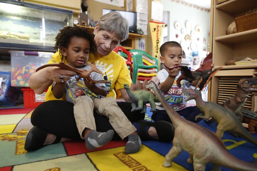 Child care provider Pat Alexander helps children, Isaiah, left, and Hector, right, identify various types of dinosaurs at her child care center in Elk Grove, Calif., on Wednesday, Feb. 26, 2020. Gov. Gavin Newsom is proposing to consolidate the state's array of child care programs and to spend up to $10 million a year to create a new Department of Early Childhood Development. The plan has gotten some criticism from some child care providers who question the wisdom of spending millions to create a new bureaucracy. (AP Photo/Rich Pedroncelli)