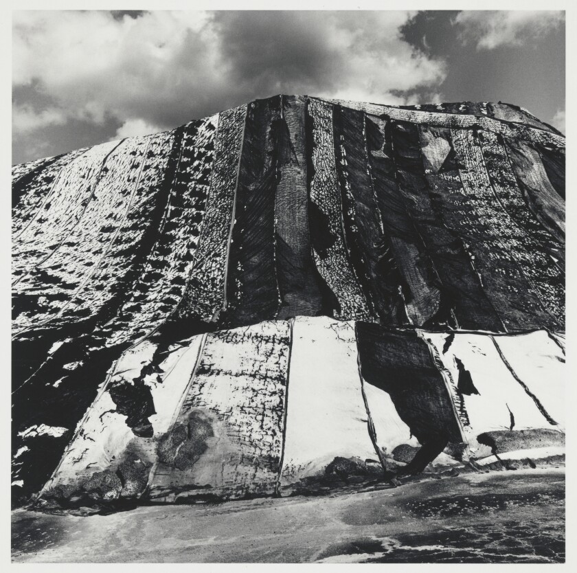 A black and white photograph of a pile of salt with a sky and clouds in the background.