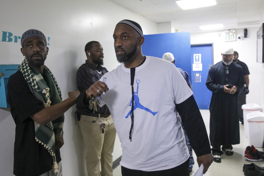 A man wearing a T-shirt with a Nike Jumpman logo walks down a hallway lined with other men