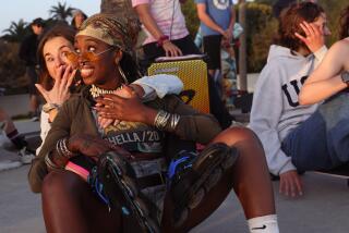 Two women sitting on a skateboard, posing for the camera.