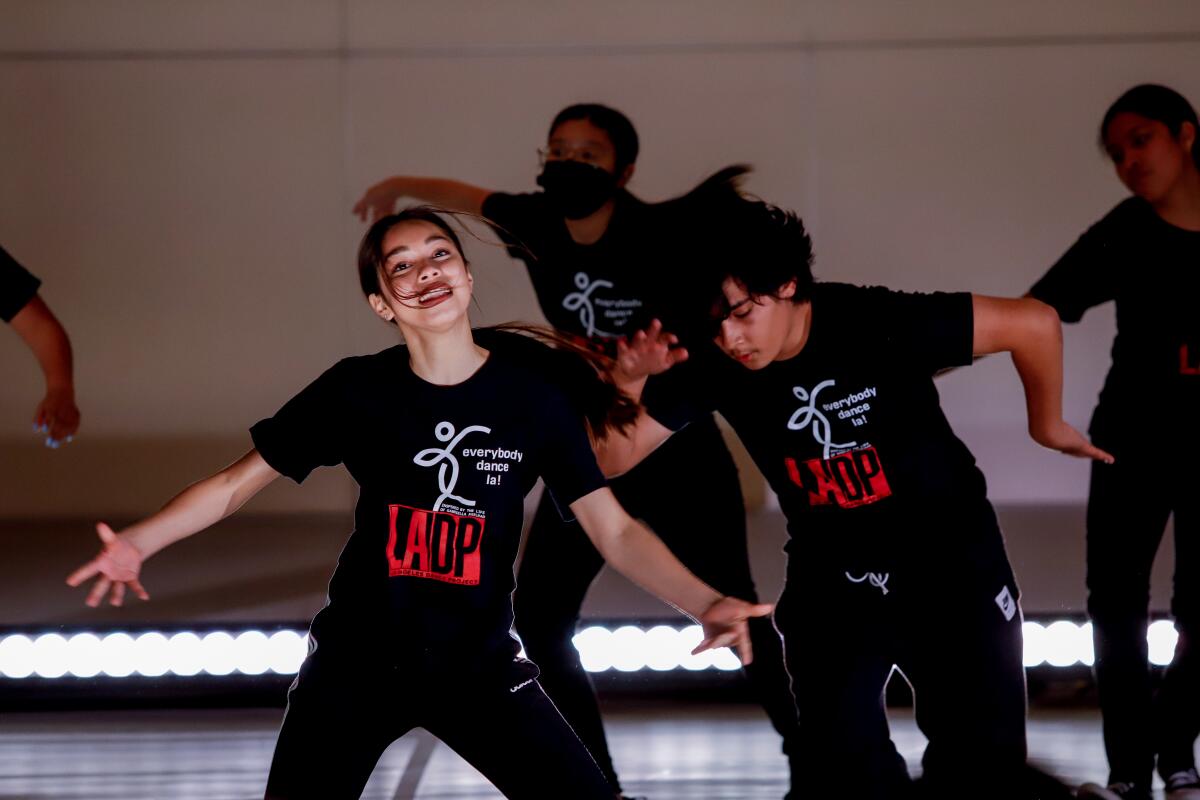 Several young people in black T-shirts that say "Everybody dance LA!" perform onstage.