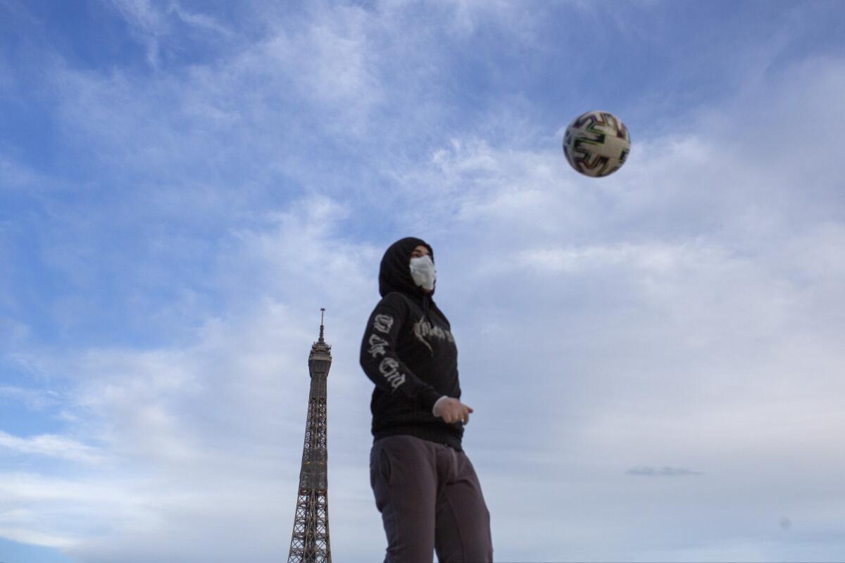 Un joven con mascarilla para evitar la propagación del coronavirus domina el balón en la plaza de Trocadero, cerca de la Torre Eiffel de París, el sábado 2 de mayo de 2020.