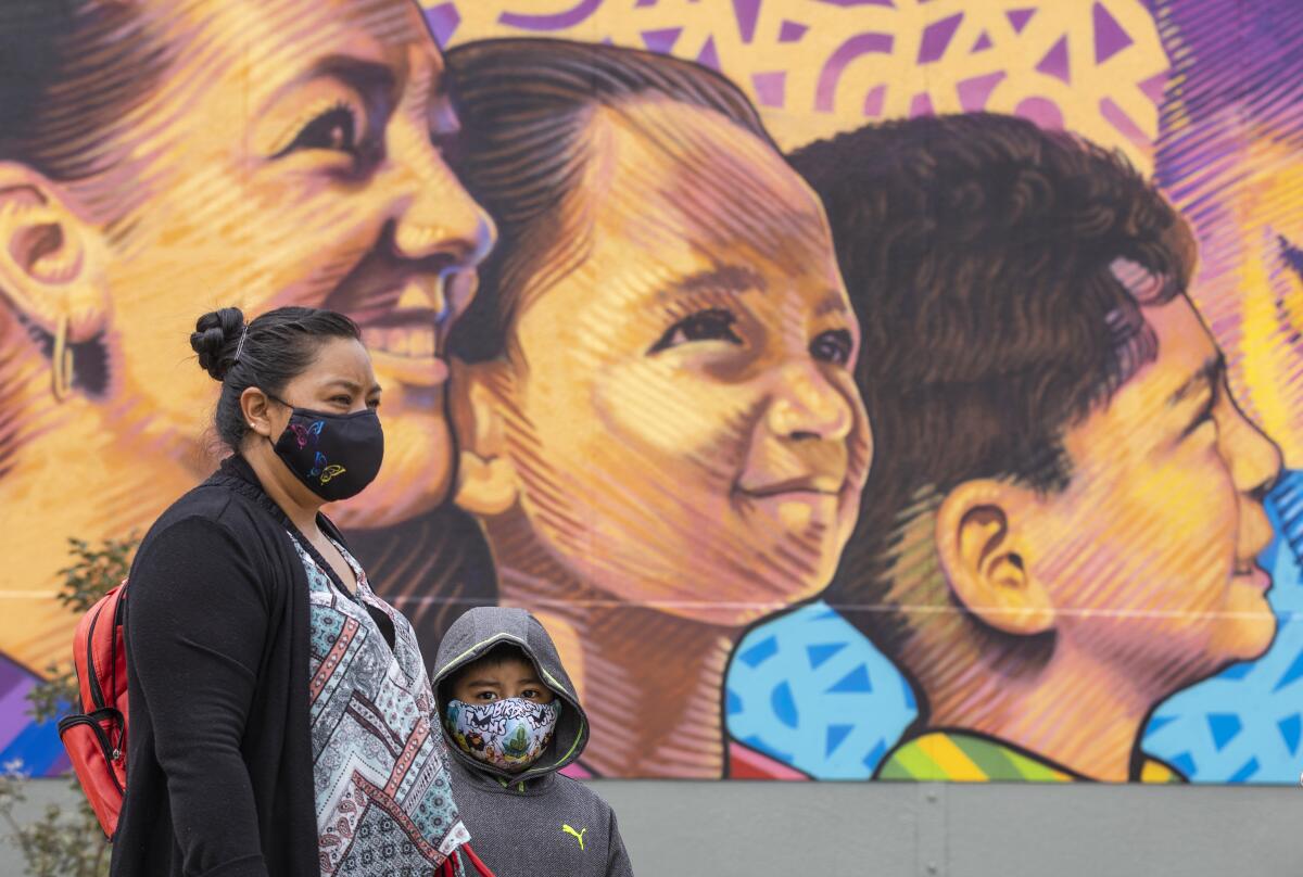A boy and his mother, both masked, stand in front of a mural