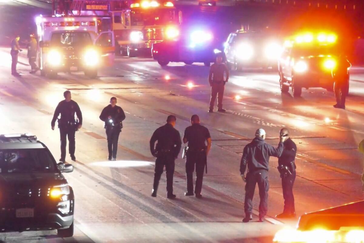 Officers stand on the freeway surrounded by emergency vehicles