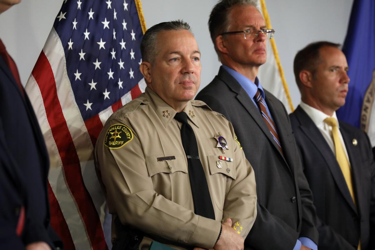 A man in a law enforcement uniform and men in suits stand in front of several flags.