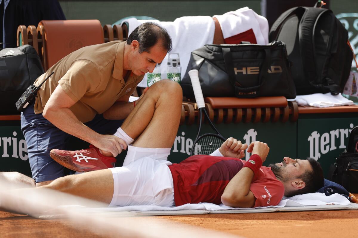 Novak Djokovic lies on the ground with one knee up.