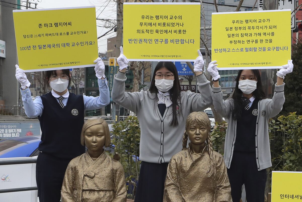 In this Feb. 25, 2021, photo, high school students hold up banners to protest a recent academic paper by Harvard University professor J. Mark Ramseyer, behind statues symbolizing wartime sex slaves in Seoul, South Korea. The signs read: "J. Mark Ramseyer, are you a 21st century professor at Harvard? Are you a university professor in the Japanese Empire 100 years ago? We criticize anti-human rights research." (Lee Jung-hoon/Yonhap via AP)