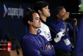 Will Ireton folds his arms while standing next to Shohei Ohtani in the Dodgers dugout 