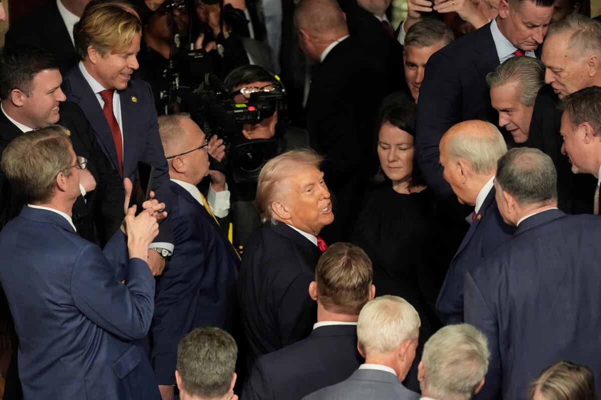 A man in a dark suit and red tie is surrounded by other people, also in suits and ties, and a woman in dark clothes