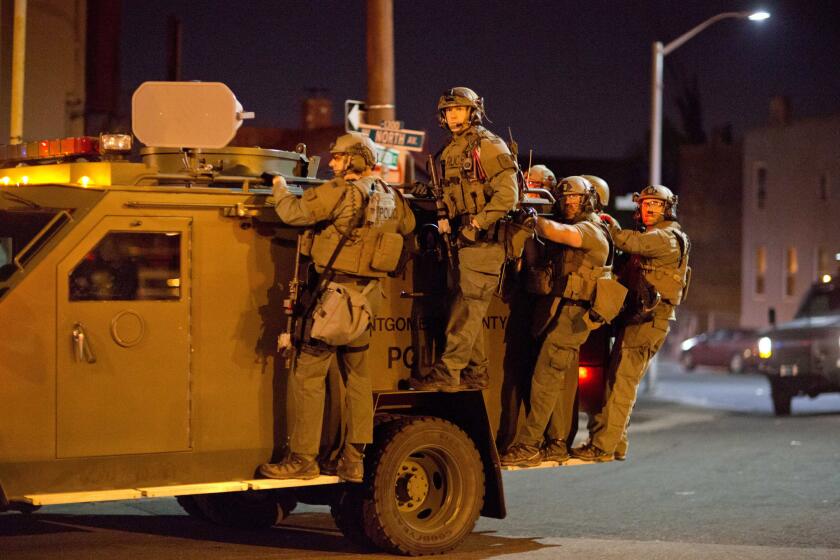 Police ride on an armored vehicle through a riot-racked area of Baltimore after a 10 p.m. curfew went into effect.