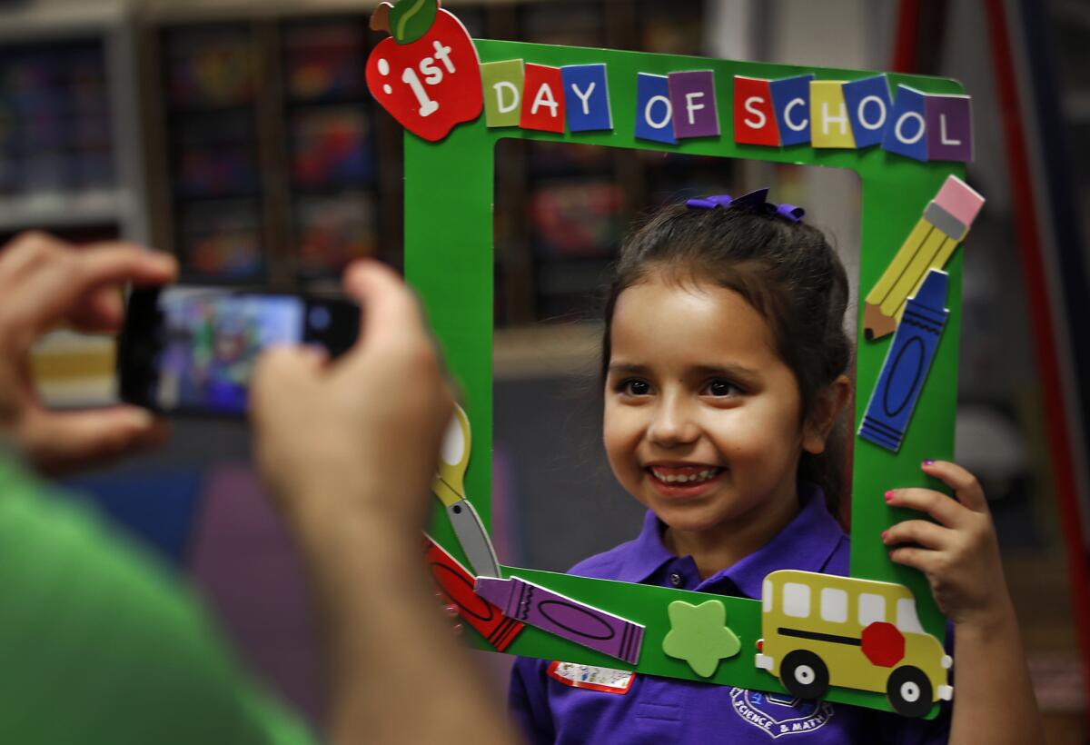 Maris Vega smiles for her father, Chris, behind a picture frame made by her teacher on the first day of kindergarten at the Telesis Academy in West Covina.