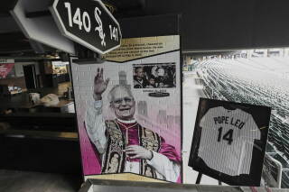 A colorful portrait of Pope Leo XIV waving appears on a wall next to a framed White Sox jersey featuring his name on its back