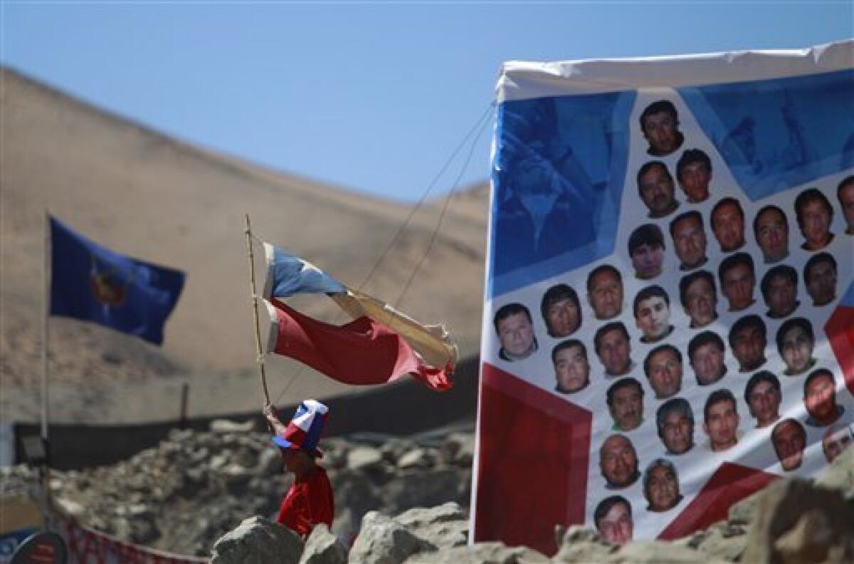 A boy holds up a flag that was used in southern Chile during February's earthquake next to images of trapped miners at the San Jose Mine near Copiapo, Chile, Tuesday, Oct. 12, 2010. Andres Sougarett, the Chilean engineer leading the rescue effort, said all would be in place at midnight Tuesday to begin the rescue of the 33 trapped miners. (AP Photo/Natacha Pisarenko)
