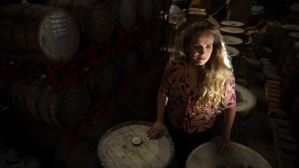 Meg Gill co-founded Golden Road Brewing and is one of the few women in the craft beer industry. She stands among ageable beer barrels.