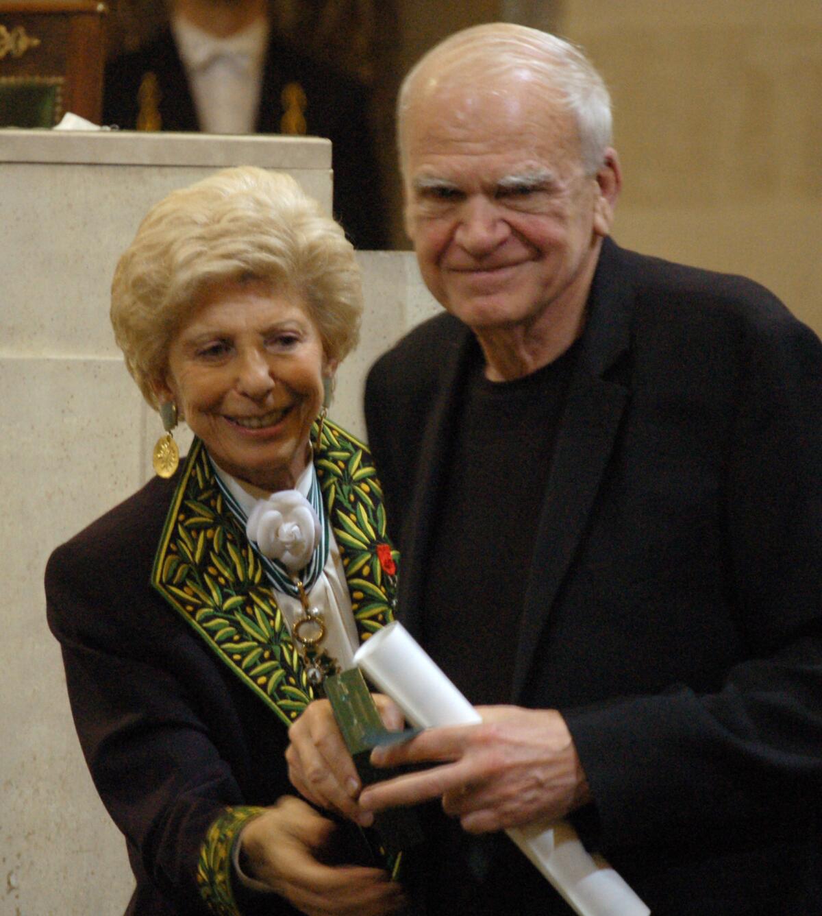 FILE - In this June 10, 2009, file photo, Czech-born author living in France Milan Kundera, right, is awarded the Simone and Cino Del Duca Foundation World Prize for his lifetime achievement in Paris, France. On the left is French political historian Helene Carrere d'Encausse. Kundera has regained Czech citizenship after 40 years, daily Pravo writes on Tuesday, Dec. 3, 2019, adding that Czech ambassador Petr Drulak handed the relevant document to him in his Paris apartment on November 28. (Remy Vlachos/CTK via AP)