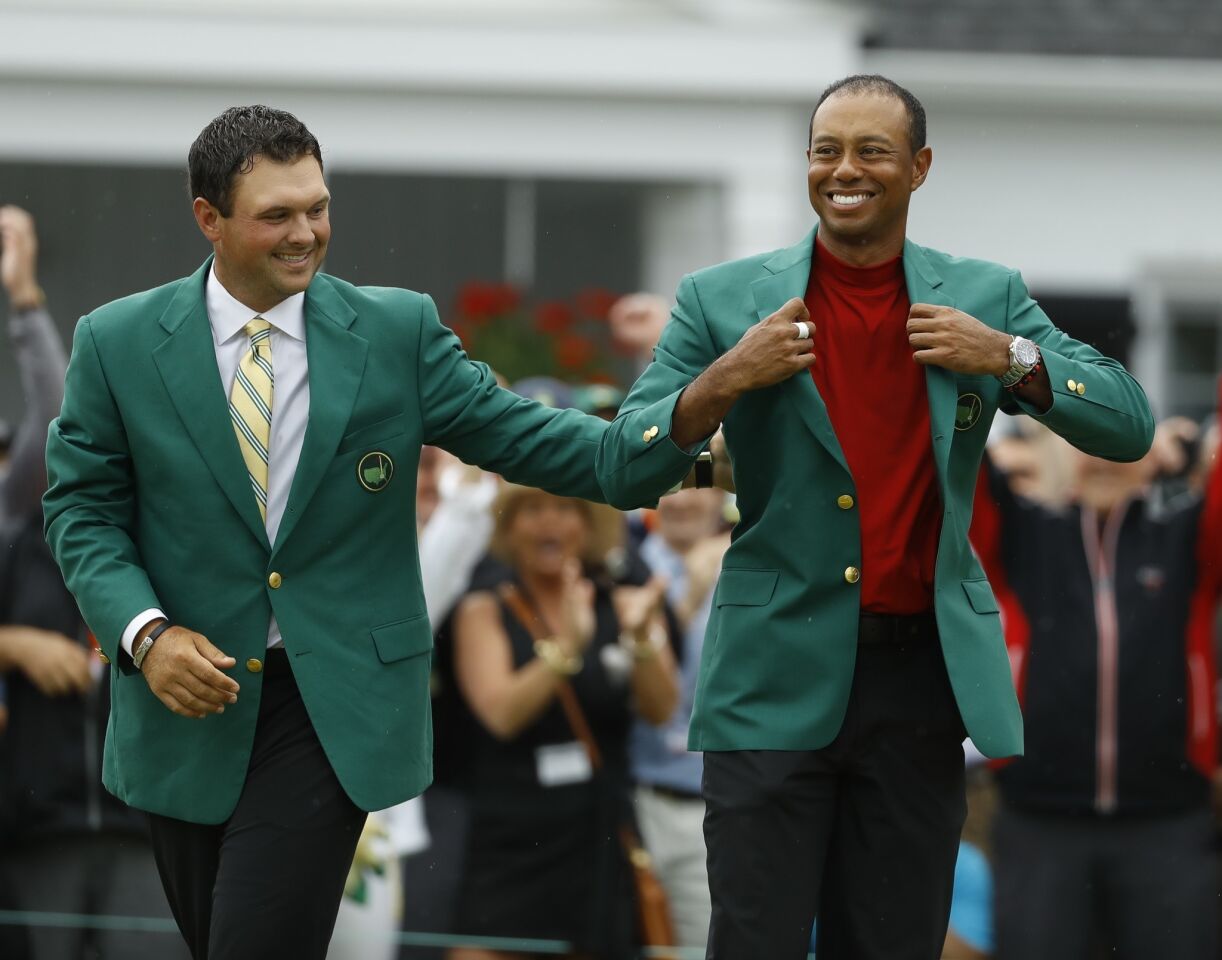 Patrick Reed, left, helps Tiger Woods with his green jacket after Woods won the Masters golf tournament Sunday in Augusta, Ga.