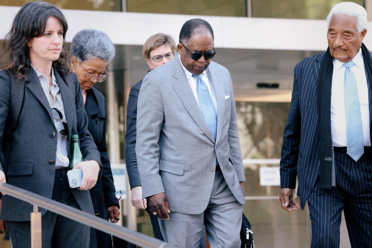 A man in a light blue suit and others walk down a flight of steps outside of a federal courthouse.