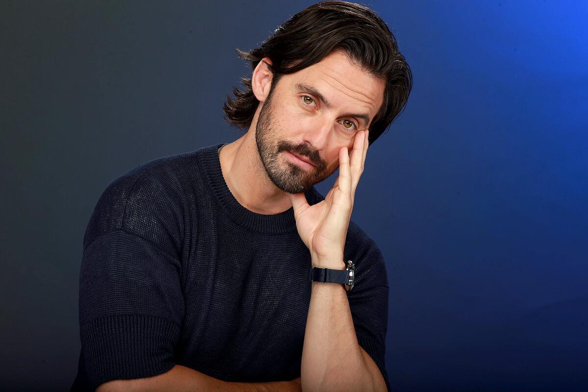 Milo Ventimiglia rests his cheek on the fingers of his open left hand and offers a barely there smile
