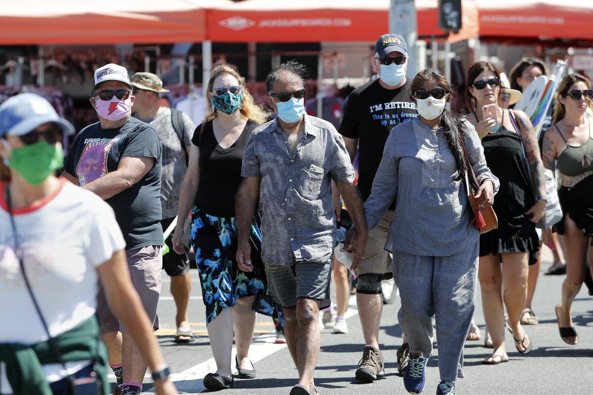 Beachgoers wear face masks to protect themselves as they walk  in downtown Huntington Beach on Saturday.