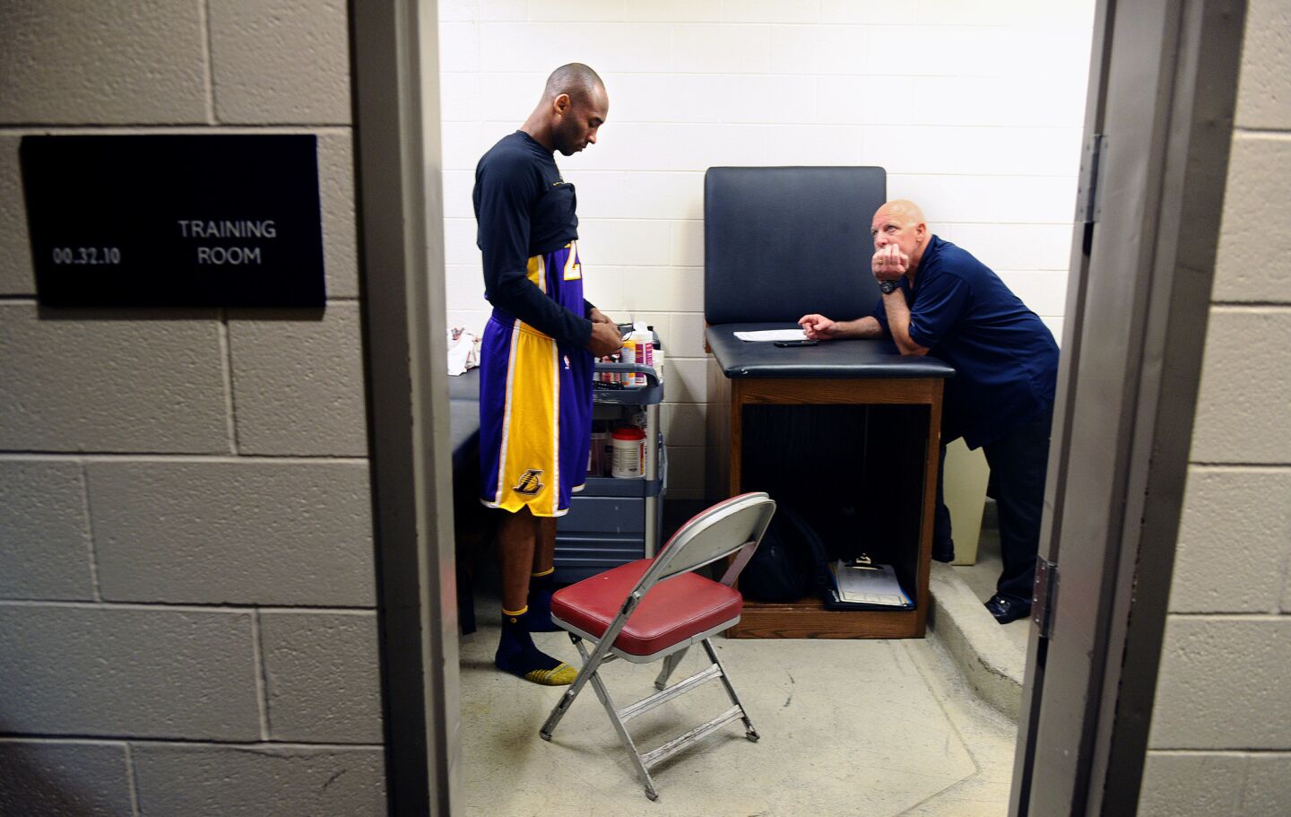 Kobe Bryant prepares for a game with the Rockets in the locker room as trainer Gary Vitti looks on in Houston.
