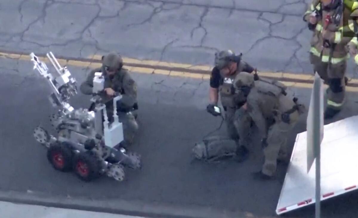 Police officers kneel by a robot.
