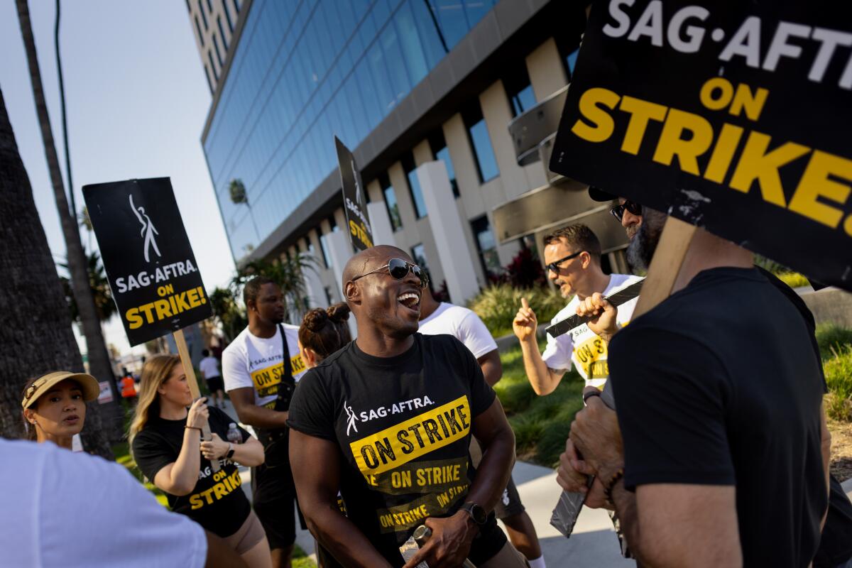 People outside a building carrying signs and wearing T-shirts that say SAG-AFTRA on Strike