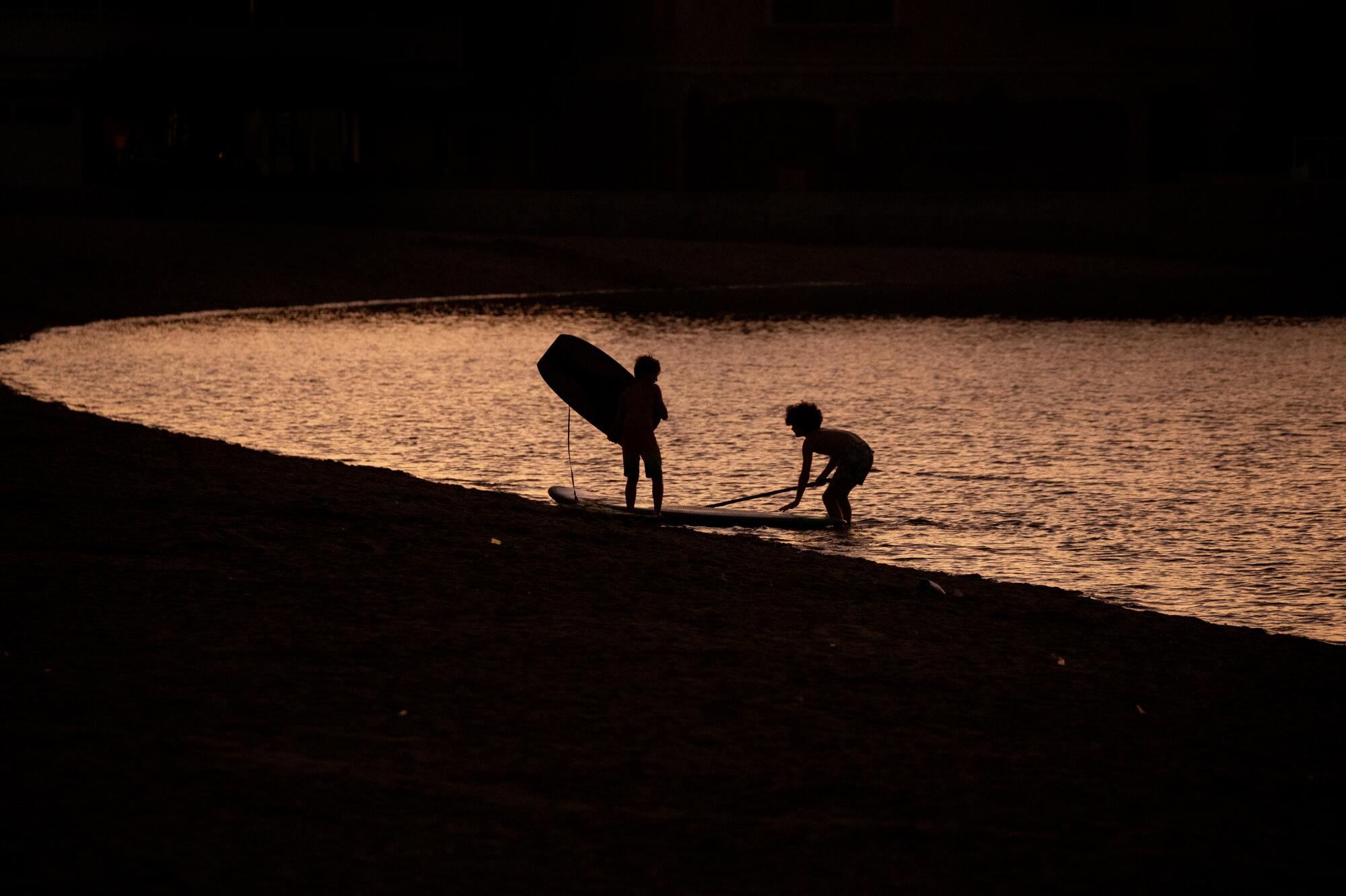 Two children play on a beach at dusk.