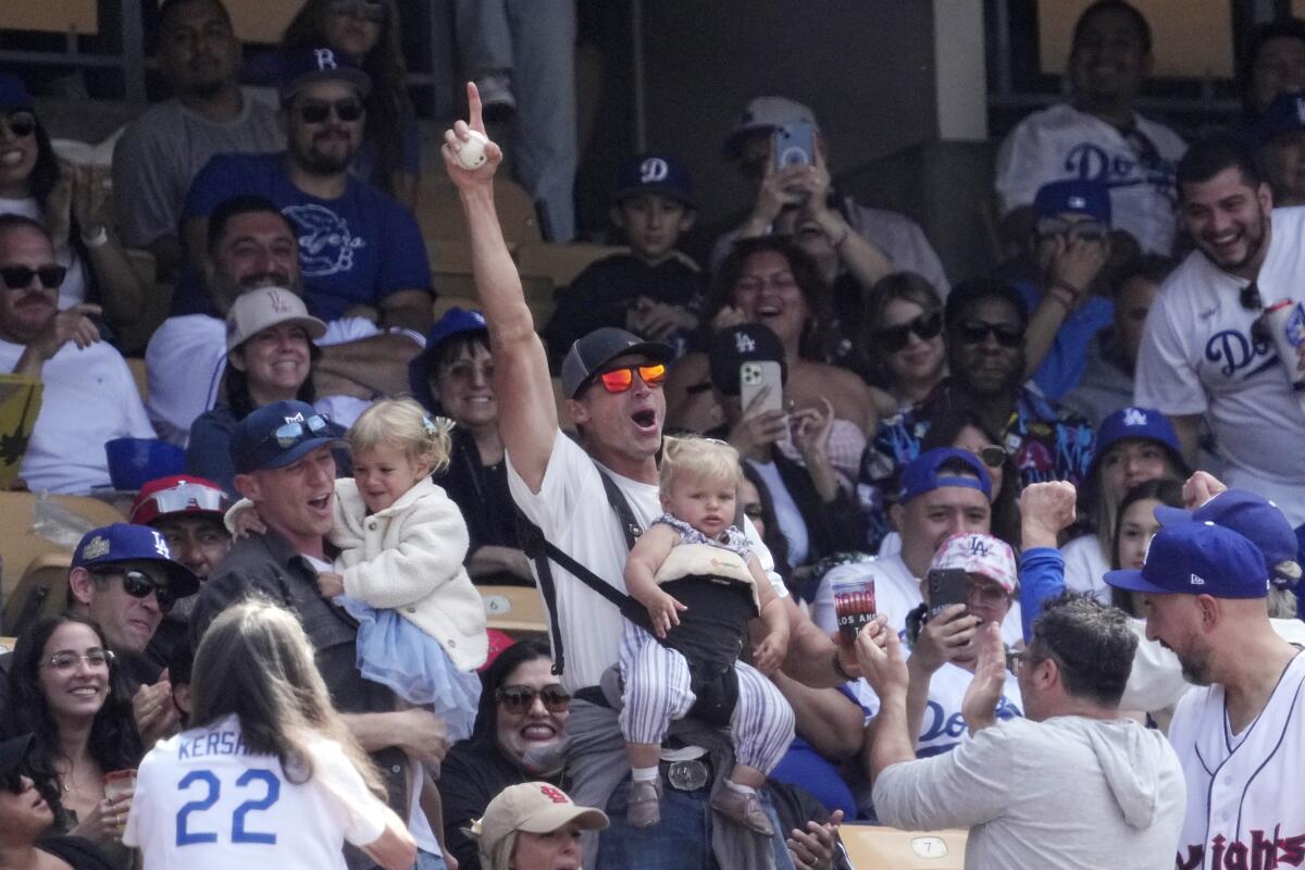 A fan celebrates after catching a foul ball while holding a toddler during the seventh inning at Dodger Stadium on Sunday.