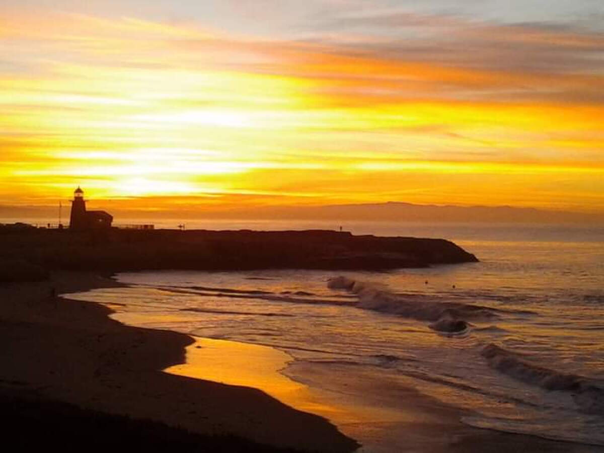 A morning sky over a rocky beach with silhouette of lighthouse.