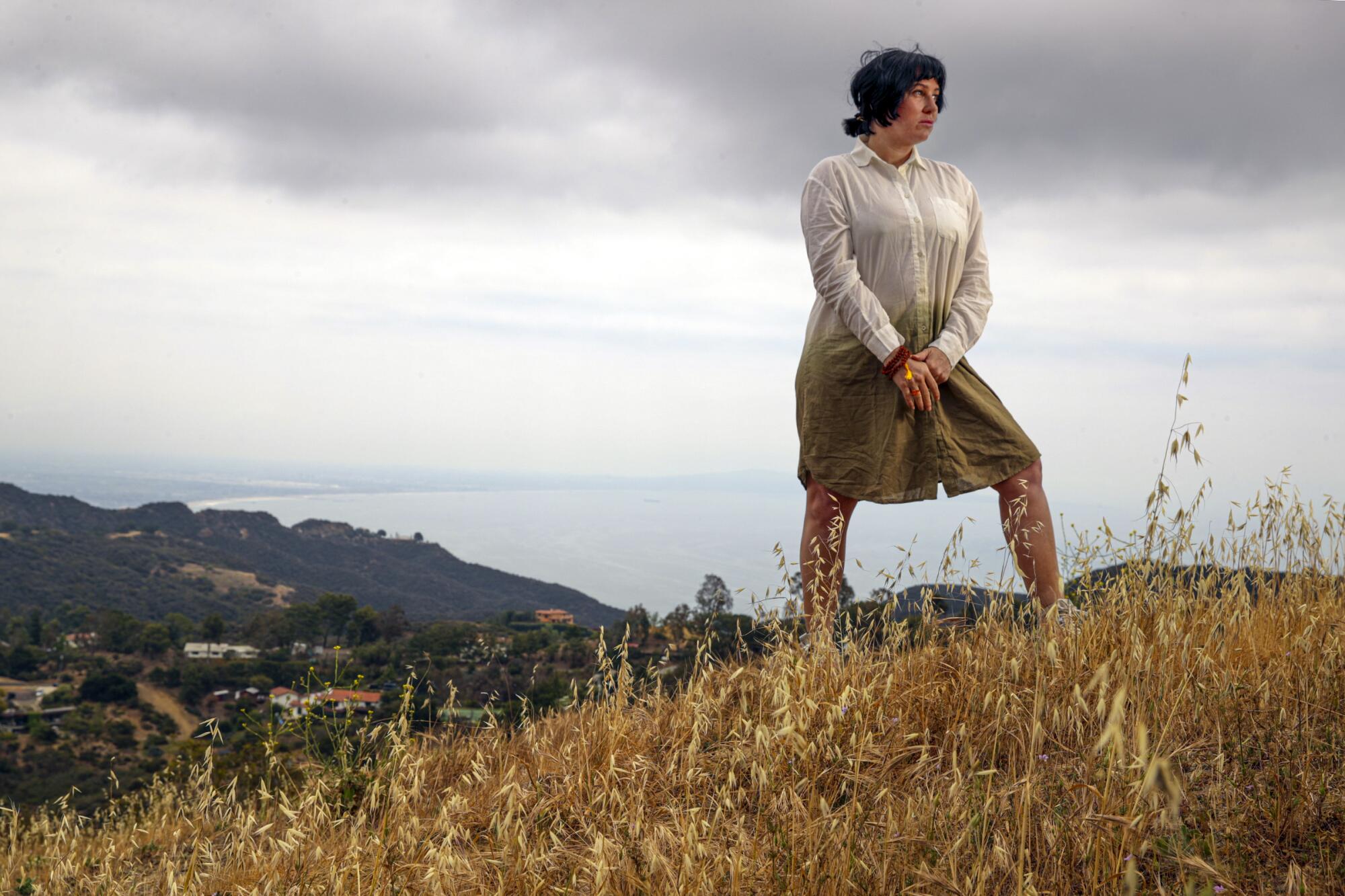 A woman stands on a hillside above the ocean.