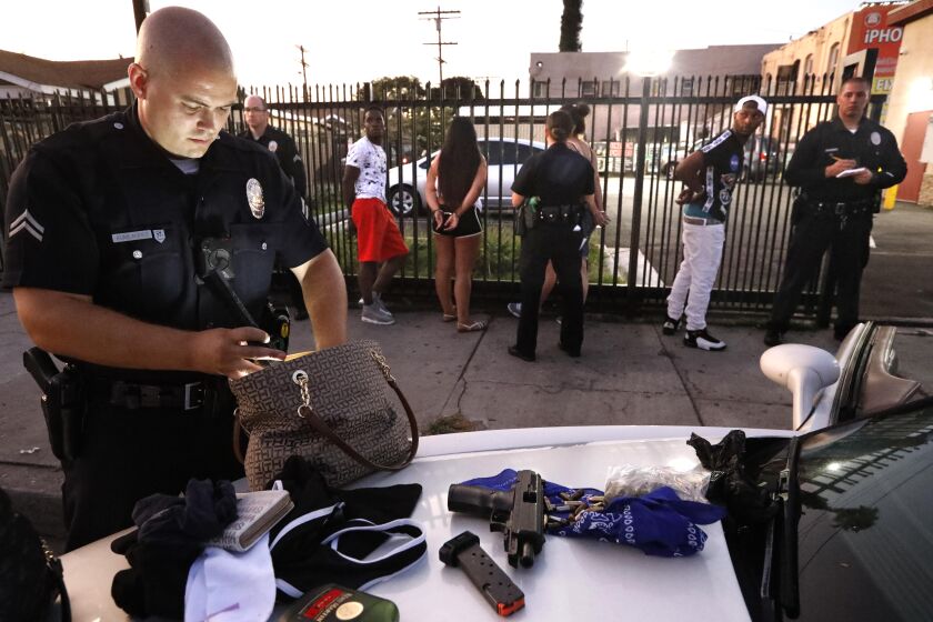 LOS ANGELES, CA - JULY 25, 2019 - - Los Angeles police officer Charles Kumlander, left, goes through the possessions of youth, handcuffed in the background, who were pulled over for acting suspiciously while driving in South Los Angeles on July 25, 2019. He found a gun and bullets on the floor of the vehicle. One of the youths was arrested for illegal possession of a firearm. (Genaro Molina / Los Angeles Times)