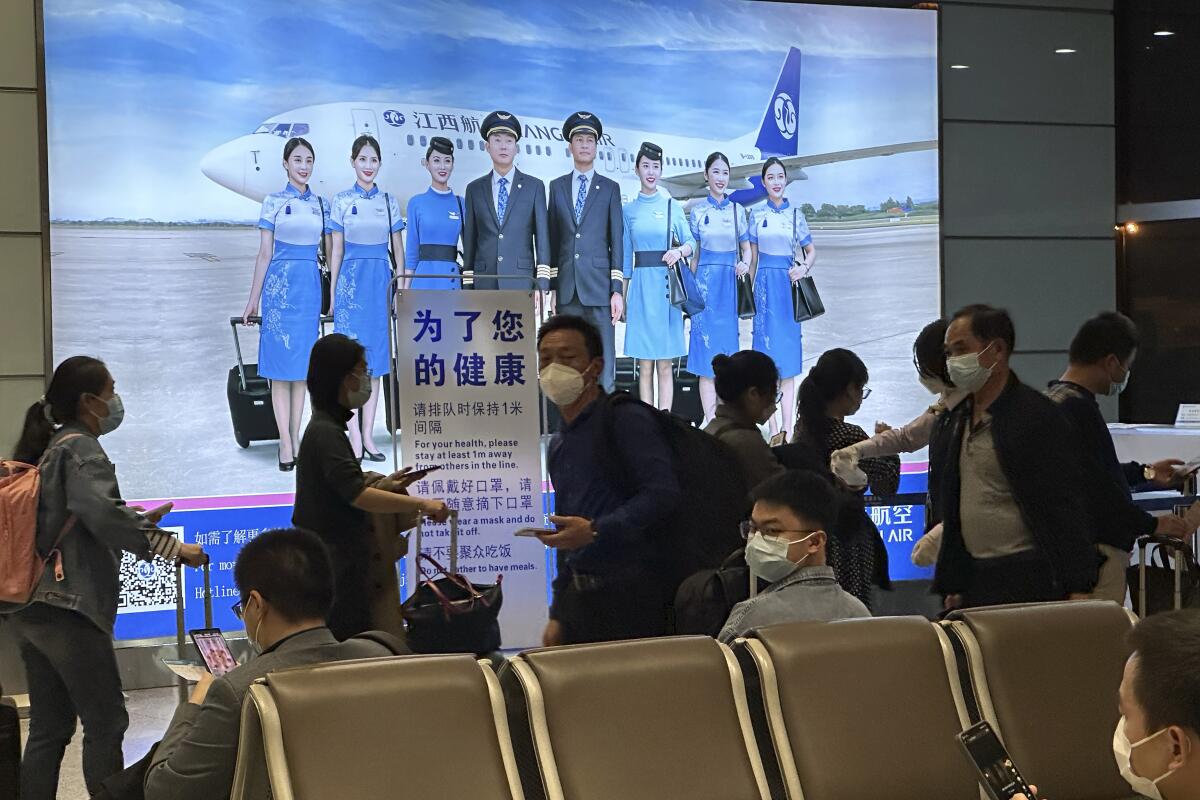 Masked people, some with luggage, pass others in seats, with a wall-sized ad depicting a flight crew and an airliner