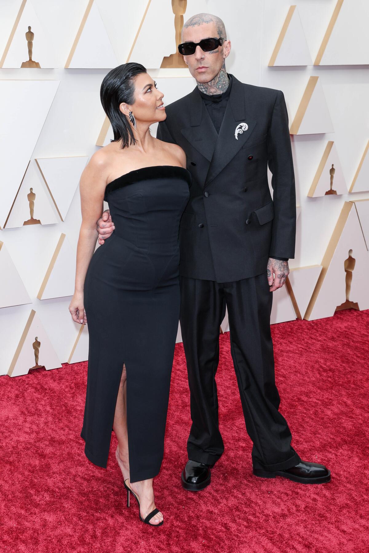 A woman with dark hair looks up at a man wearing sunglasses and a dark suit on a red carpet.