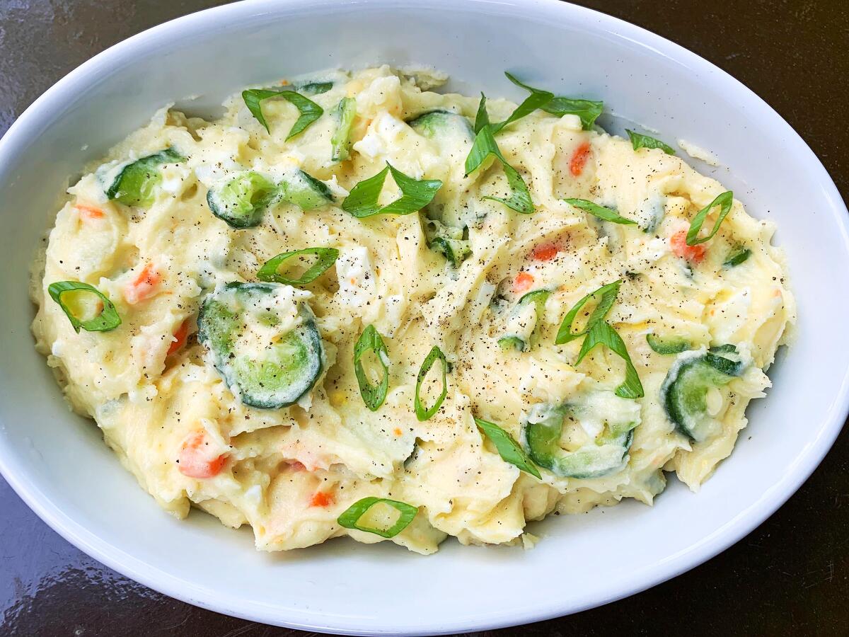 Slice of cucumber and green onion are seen in a dish of creamy potato salad.