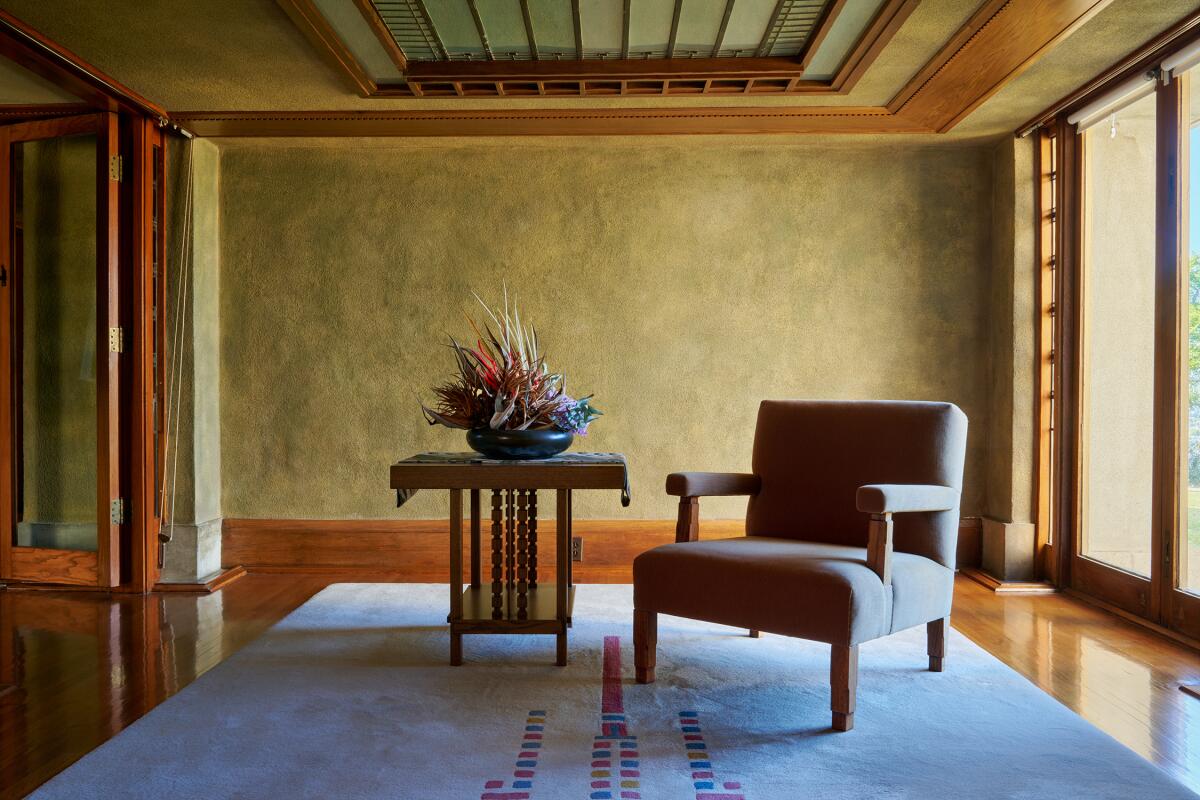 A  simply furnished room in Hollyhock House, with a padded arm chair, side table and abstract ikebana floral dislay