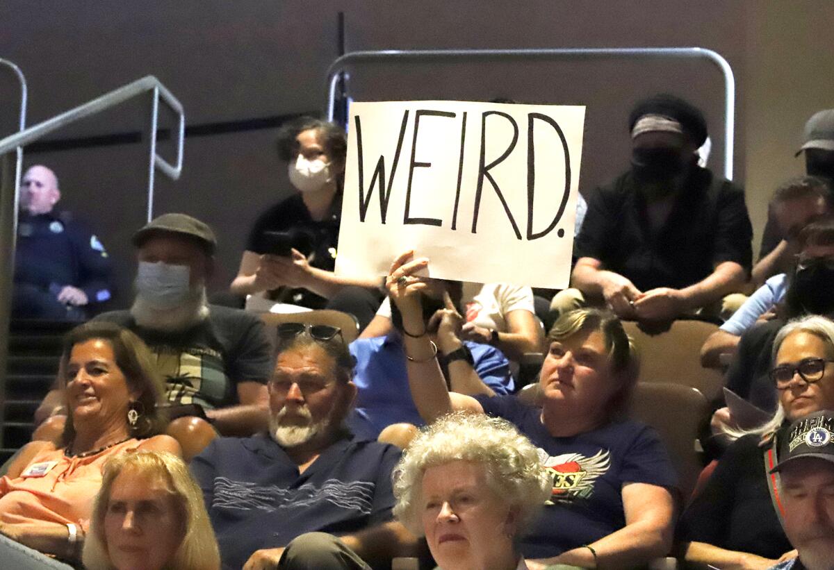 Buffie Channel holds a sign reading "weird" during public comments at Tuesday night's Huntington Beach City Council meeting.